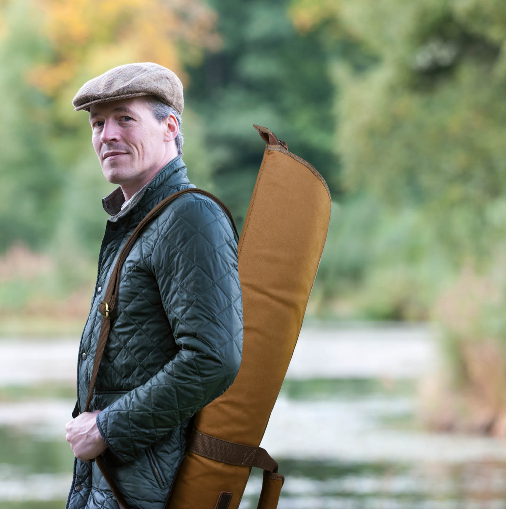 man carrying hunting rifle hunter carrying rifle on shoulder standing on riverbank looking at the camera
