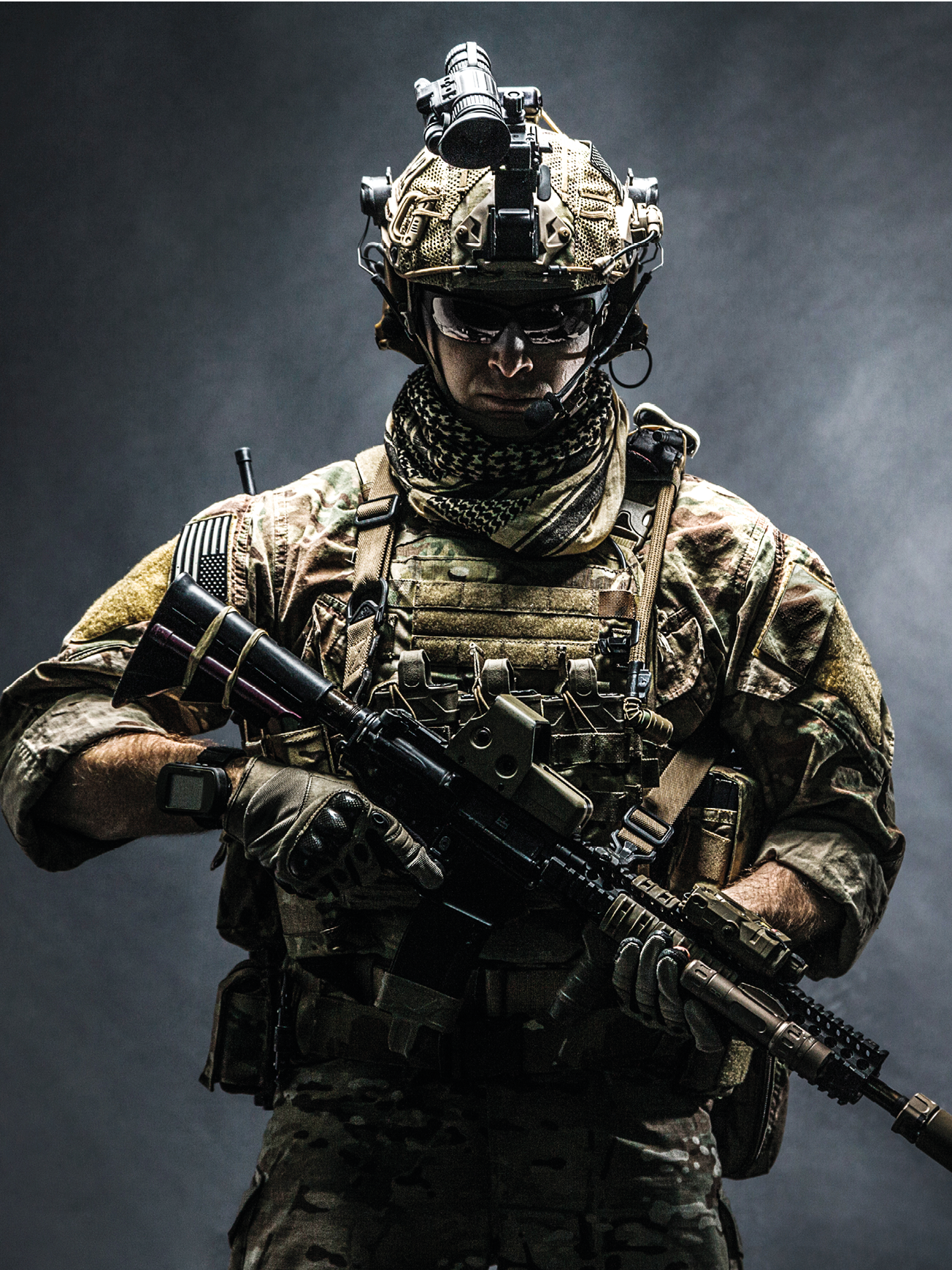 Army soldier in Combat Uniforms with assault rifle, plate carrier and combat helmet are on, Shemagh Kufiya scarf on his neck. Studio shot, dark background